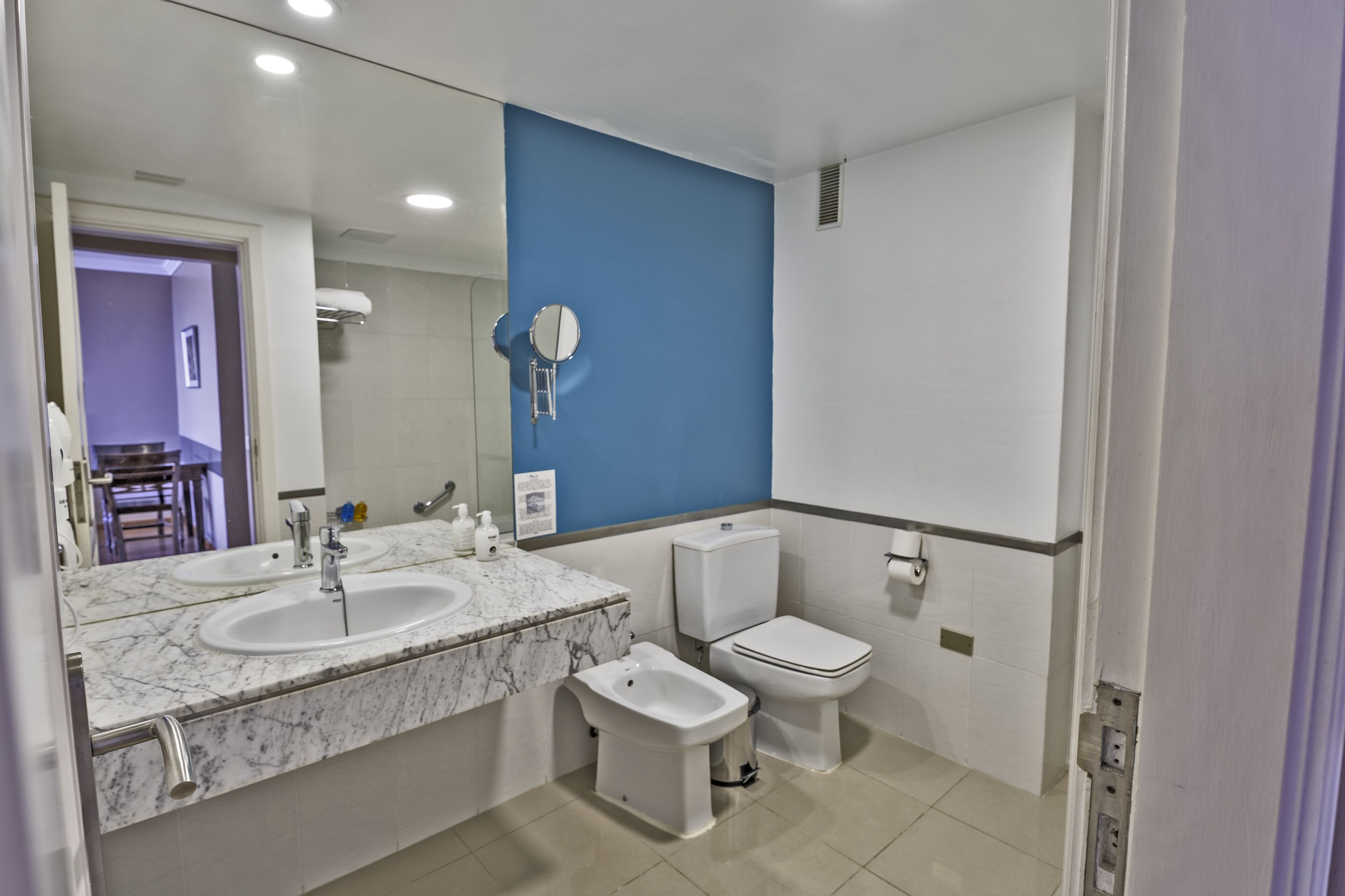A bathroom with two sinks, a bidet, a toilet, and a mirror.