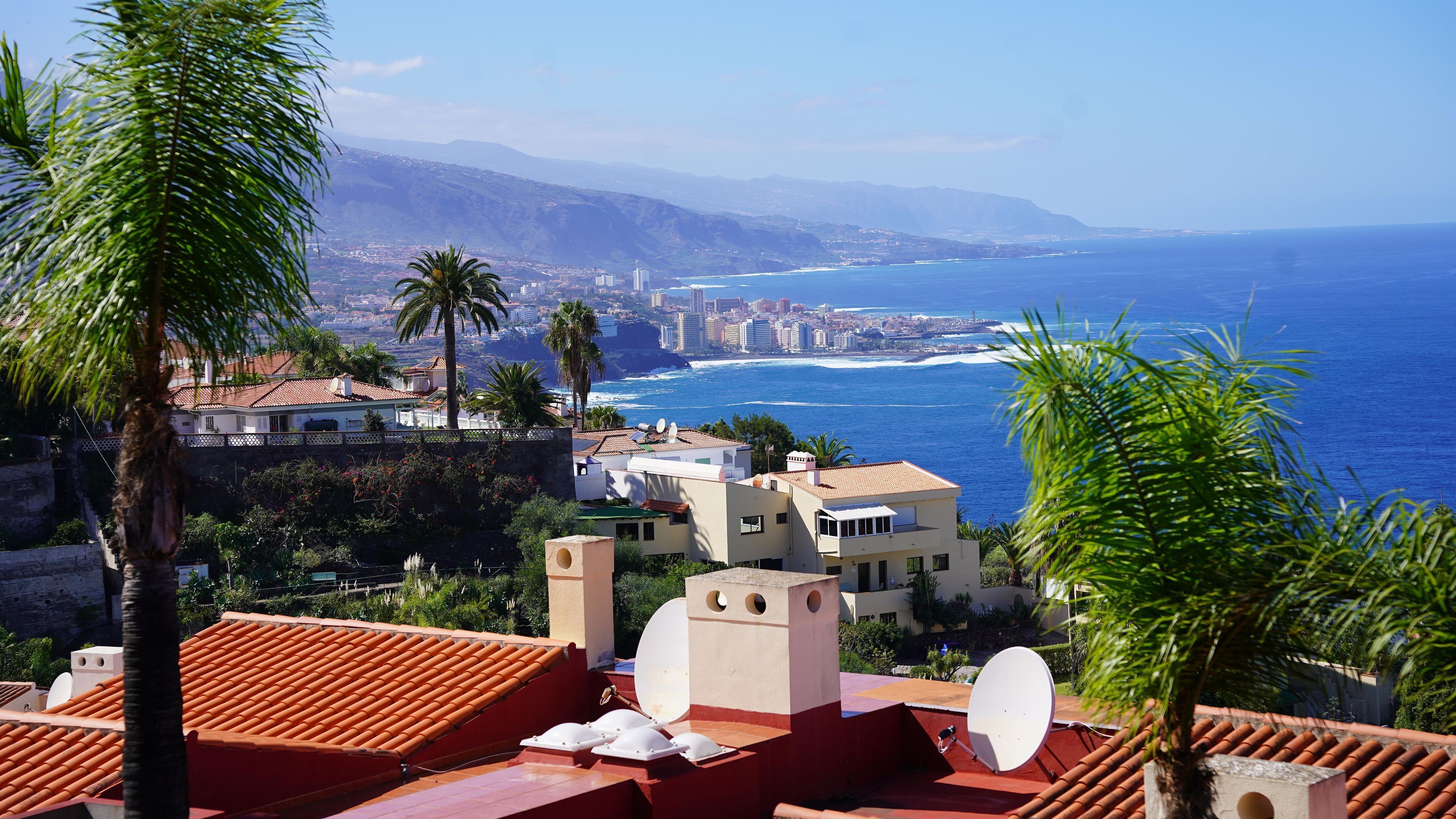 A coastal cityscape with buildings, a beach, and mountains in the background.