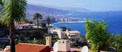 A coastal cityscape with buildings, a beach, and mountains in the background.