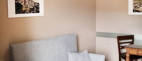 Una habitación con un sofá gris, una mesa de comedor de madera y dos cuadros en la pared.