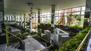 Un atrium intérieur moderne, doté d’un escalier central et entouré de plantes et de murs en pierre.