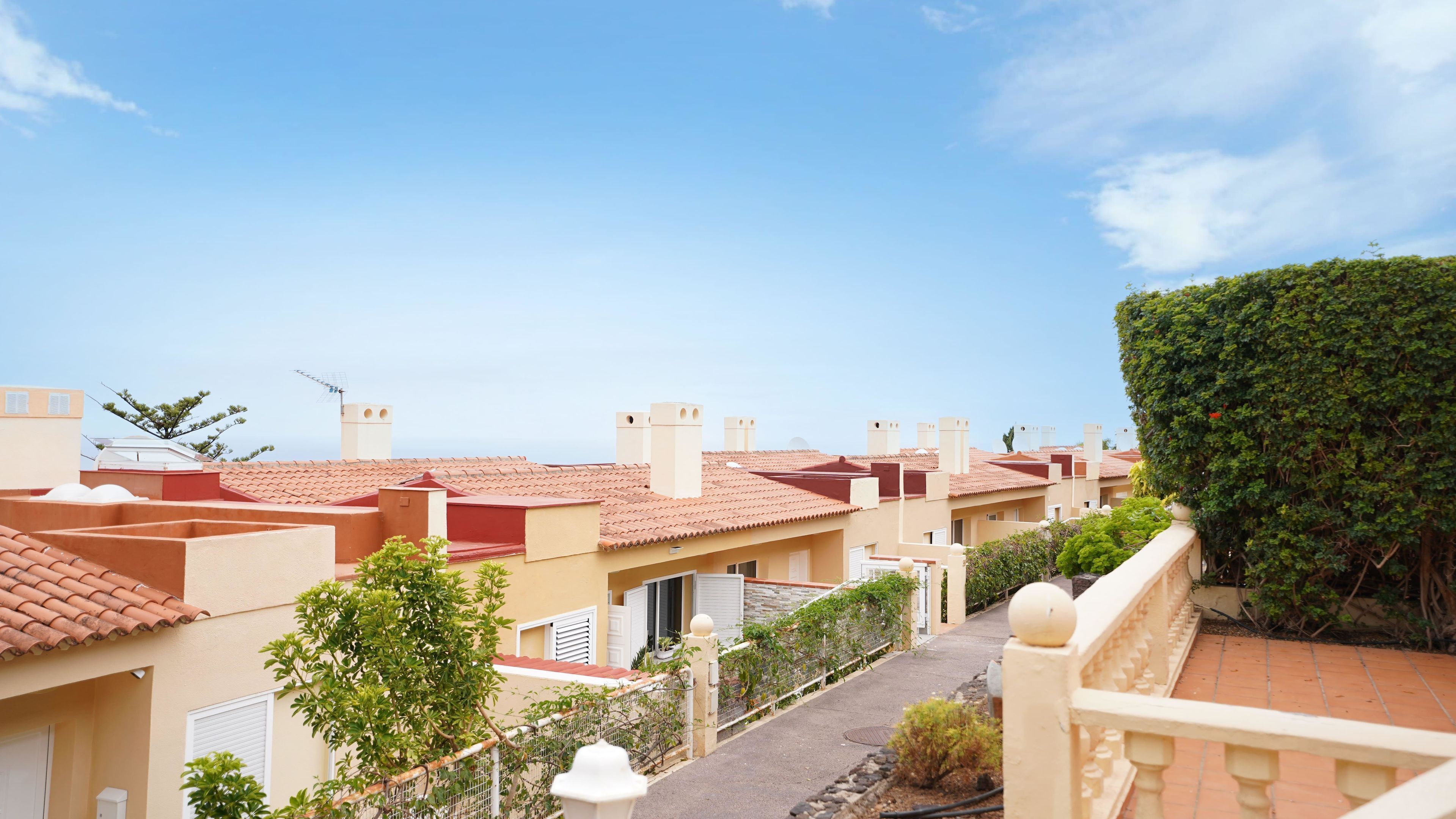 Zona residencial con tejados de tejas de arcilla, un sendero y un seto.