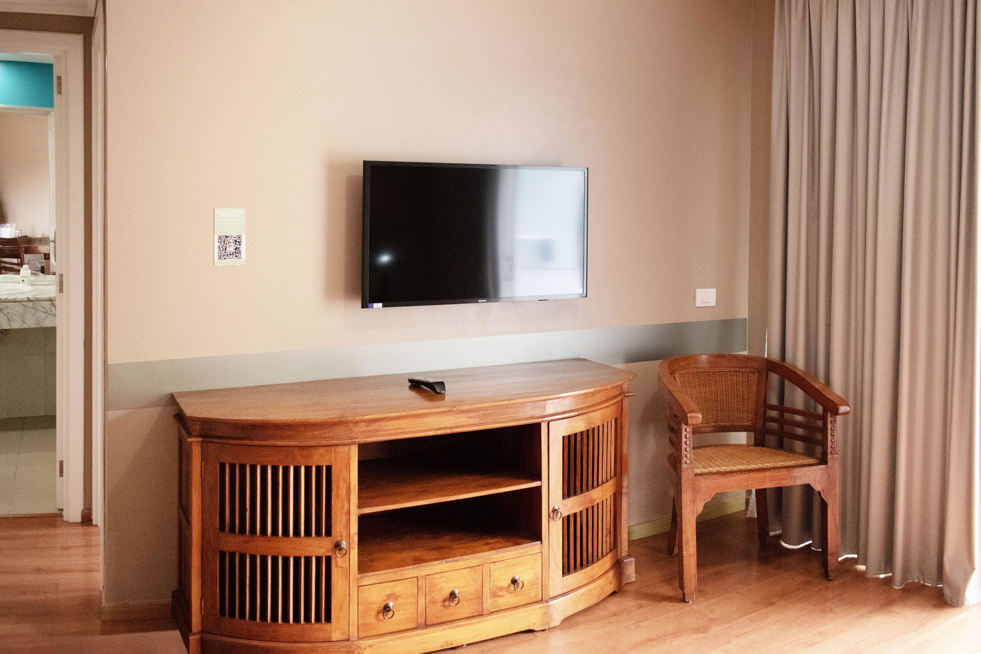 A wooden entertainment unit with a flat-screen TV, a chair, and a door leading to another room.