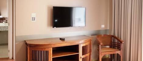 A wooden entertainment unit with a flat-screen TV, a chair, and a door leading to another room.