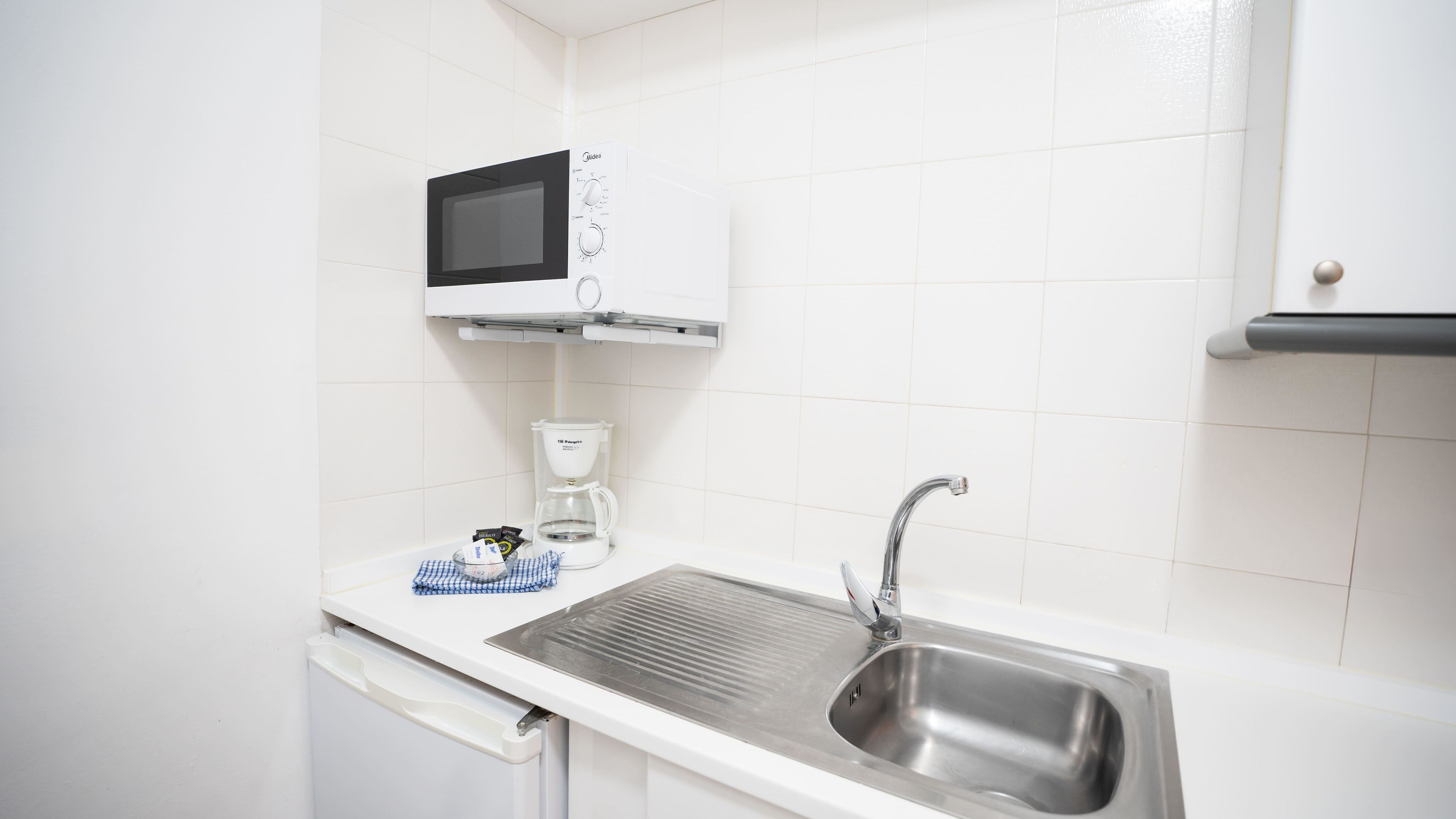 Una cocina equipada con microondas, cafetera, lavaplatos y fregadero.