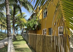 A yellow building with a wooden fence, palm trees, and a clear sky.