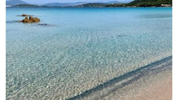 Ein heller Strand mit flachem Wasser und einer fernen Bergkette.
