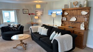 A living room with two black sofas, a wooden coffee table, and a wooden cabinet with decorative items. - Welcoming 2 Bed Charming Self Catering Cottage (Cheddar)