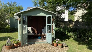 A small, open shed with a door open, revealing a chair and a table inside. - Welcoming 2 Bed Charming Self Catering Cottage (Cheddar)