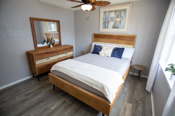 A bedroom with a wooden bed, a dresser, a mirror, and a ceiling fan.