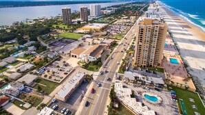 An aerial view of a coastal city with high-rise buildings, a beach, and a parking lot.