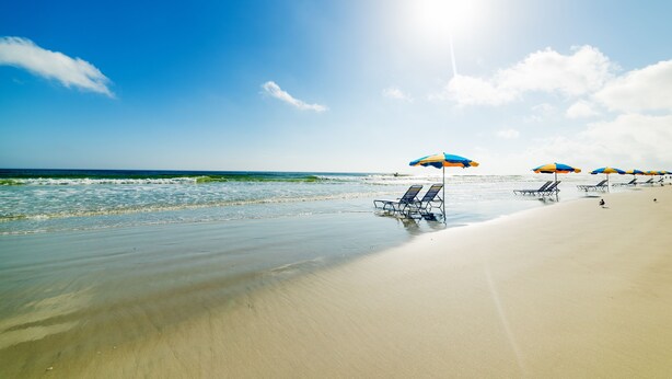A beach with clear skies, ocean waves, and beach umbrellas.