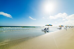 A beach with clear skies, ocean waves, and beach umbrellas.