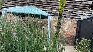 A garden area with tall grass, a blue canopy, and a brick wall. - Studio Annex (Cambridge)