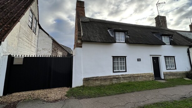 A white building with a black door and windows, a brick chimney, and a black fence. - Studio Annex (Cambridge)