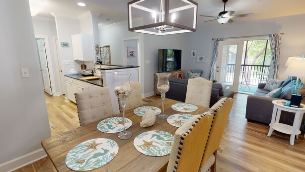 A modern living room with a wooden dining table, a sofa, and a TV. - Gorgeous 3BR Condo in FOLEY near OWA/THE BEACH!! (Foley)