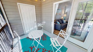 A sunlit patio with a white table and chairs, a sliding glass door leading to a living room with a sofa and cushions. - Gorgeous 3BR Condo in FOLEY near OWA/THE BEACH!! (Foley)