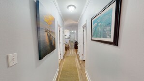 A hallway with a wooden floor, white walls, and framed pictures on the walls. - Gorgeous 3BR Condo in FOLEY near OWA/THE BEACH!! (Foley)