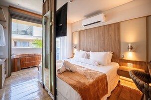 Una habitación de hotel con una cama, cabecera de madera, unidad de aire acondicionado, mesita de noche y una silla.