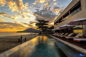 A poolside area with lounge chairs and umbrellas, overlooking a beach and ocean at sunset. - Duke Beach Hotel & SPA Maresias (São Sebastião)