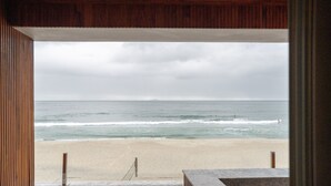 A beach view from a wooden-framed window overlooking a sandy beach with waves. - Duke Beach Hotel & SPA Maresias (São Sebastião)