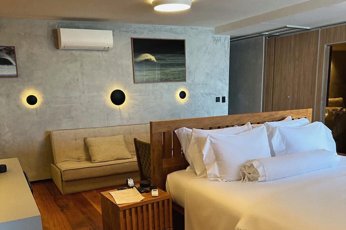 Una habitación de hotel moderna con una cama grande, un sofá, una mesita de madera y un aire acondicionado de pared.