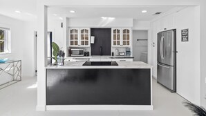 Een moderne keuken met witte kasten, een zwart eiland, roestvrijstalen apparatuur en uitzicht op de woonkamer.