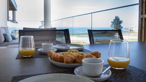 A breakfast setting with croissants, orange juice, and coffee on a balcony overlooking the ocean.