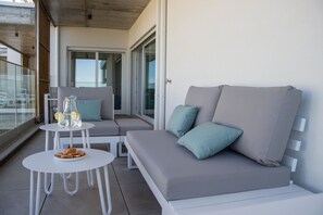 Ein Balkon mit einer grauen Couch, zwei weißen Tischen und einer Glastür, die zu einem Außenbereich führt.