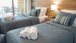 A hotel room with two beds, a wooden headboard, a bedside table with a lamp, and a view of the outside.