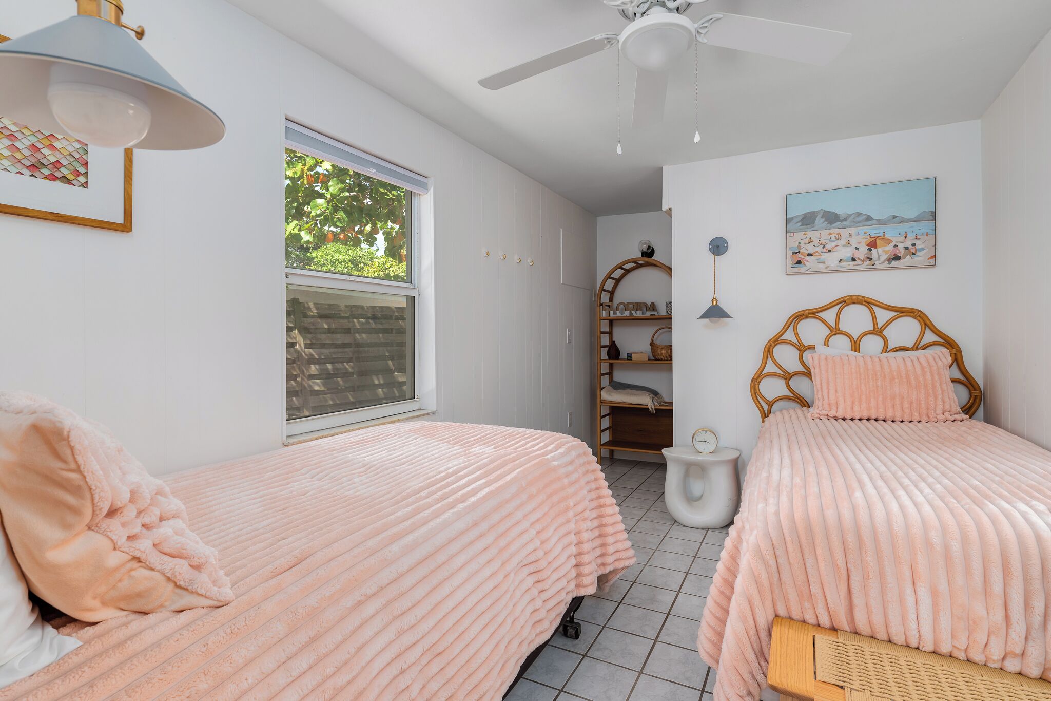 A bedroom with two beds, a ceiling fan, a window, and a shelf with items.