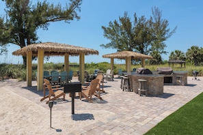 Un patio al aire libre con sombrillas de paja, sillas de madera y una zona de barbacoa.