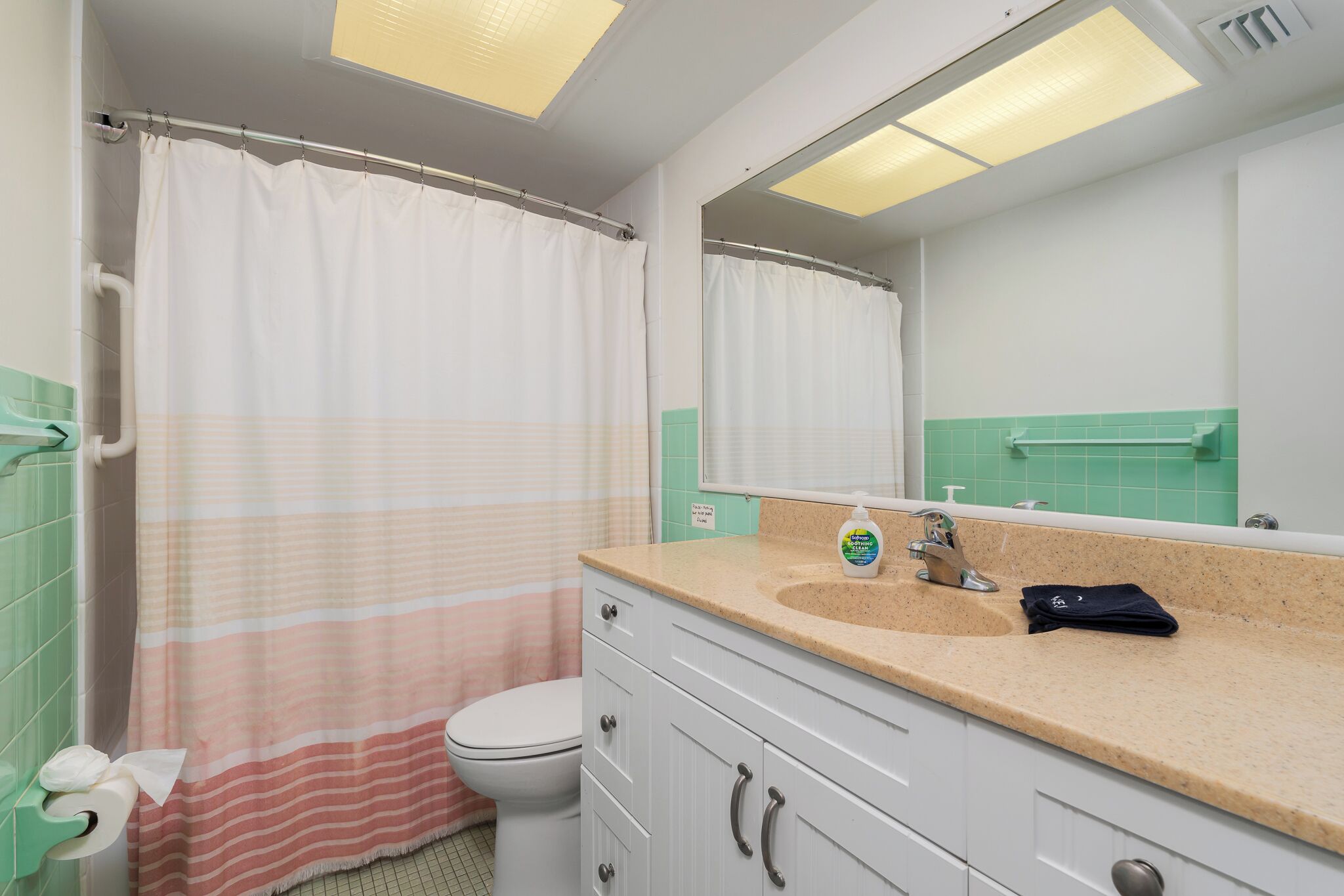 Une salle de bain avec des toilettes blanches, un lavabo beige avec un miroir au-dessus, et un rideau de douche.