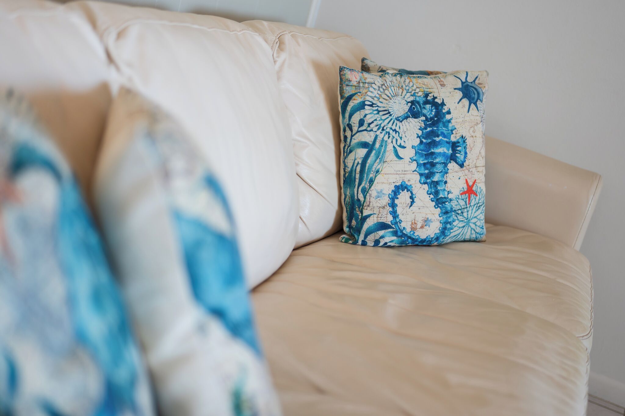 A beige sofa with a decorative pillow featuring a seahorse design.
