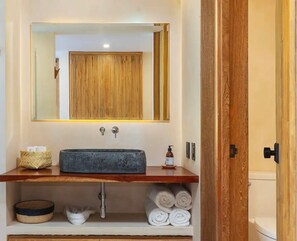 Un baño con tocador de madera, un espejo grande, un lavabo y un inodoro visible a través de una puerta entreabierta.