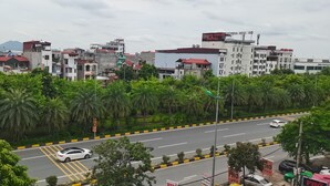 A cityscape with a road lined with palm trees, buildings with red roofs, and a white car driving. - Thanh Huong 99 Hotel - Noi Bai (Hanoi)