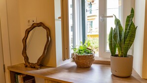 A wooden console table with a mirror, a potted plant, and a bookshelf with books. - Captivating 1-bed Apartment in Kerkira (Corfu)