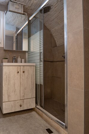 A bathroom with a wooden vanity, a glass shower enclosure, and a tiled floor.