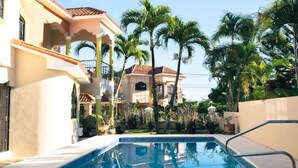 A swimming pool area with a clear view of a building with a tiled roof and a balcony. - Peaceful culdesac orchid villa, pool, work ergo (Puerto Plata)
