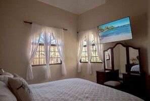 A bedroom with a bed, two windows with curtains, a television, and a dresser. - Peaceful culdesac orchid villa, pool, work ergo (Puerto Plata)