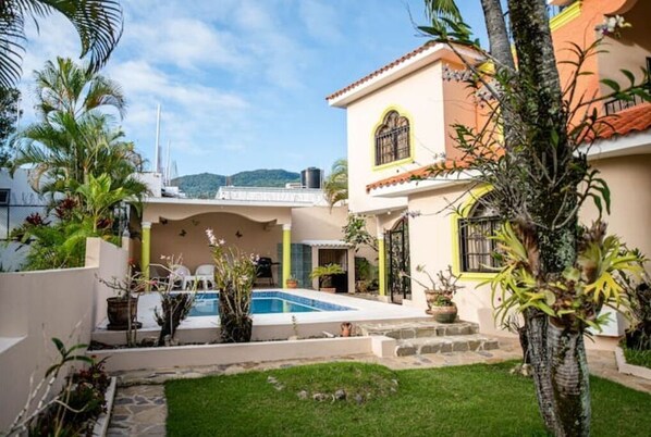 A two-story house with a swimming pool, surrounded by greenery and a clear sky. - Peaceful culdesac orchid villa, pool, work ergo (Puerto Plata)