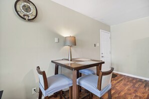 A dining area with a table, two chairs, a lamp, and a wall clock.