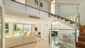 A modern interior with a wooden staircase, a glass railing, and a white sofa with yellow cushions.