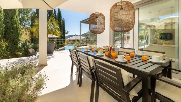 A dining area with a table set for breakfast, overlooking a swimming pool and lush greenery.
