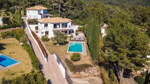 A two-story house with a swimming pool, surrounded by trees and a mountain in the background.