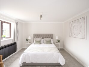 A bedroom with a bed, bedside tables, a radiator, a window with curtains, and a wall art piece.