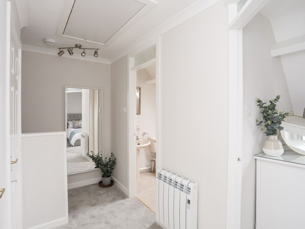 A hallway with a radiator, a potted plant, and a mirror reflecting a bedroom.
