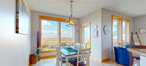 A spacious dining area with a view of the outdoors, large windows, and a modern chandelier. - Sand Dollar Shores at Seaside Beach - Pet Friendly! (Seaside)