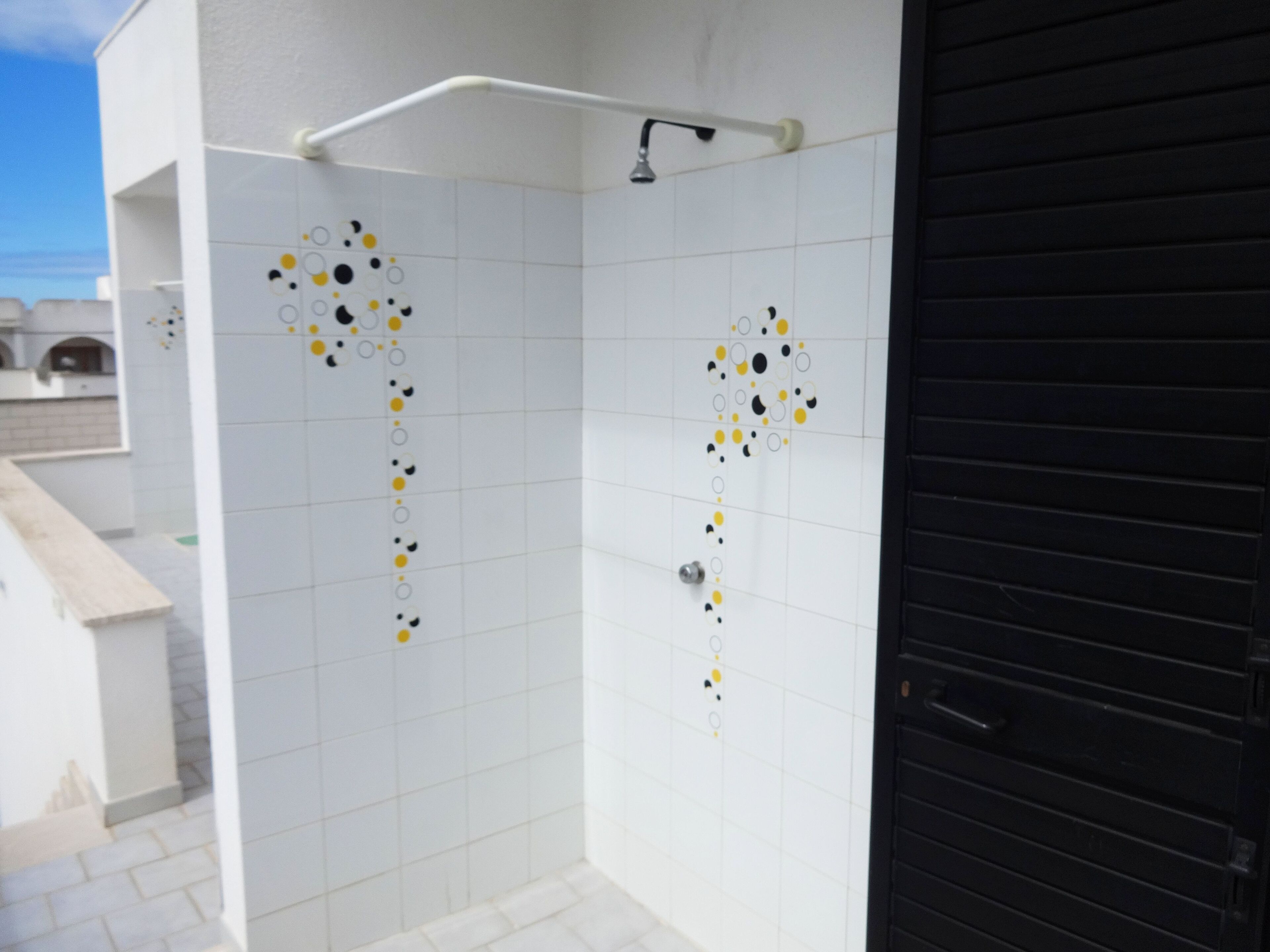 Un área de ducha con azulejos en una combinación de blanco y negro, un cabezal de ducha y una puerta.