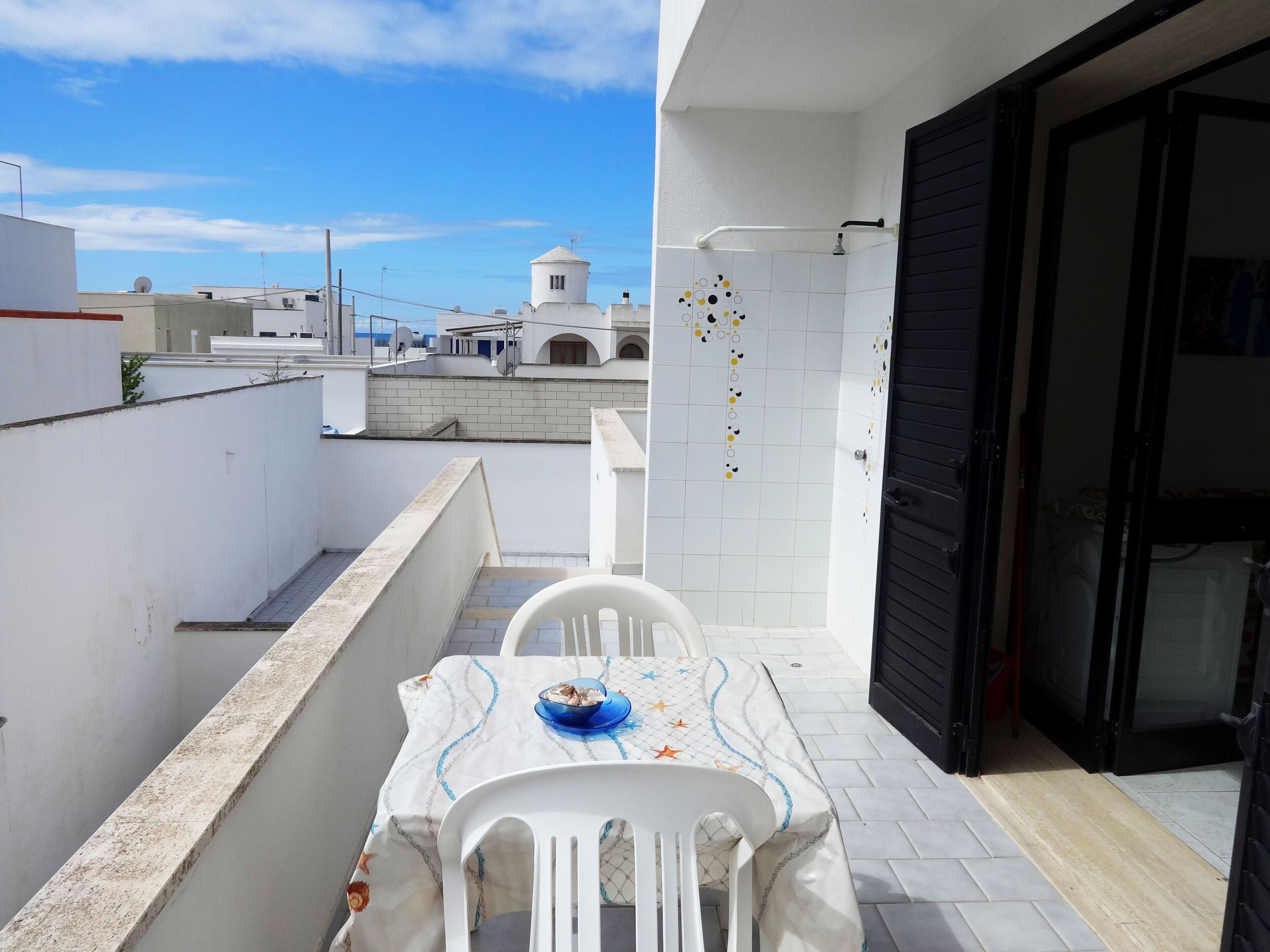 A balcony with a table set for two, a white chair, and a blue bowl.